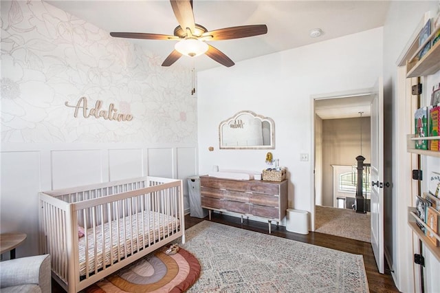 bedroom with a crib, dark wood-type flooring, and ceiling fan