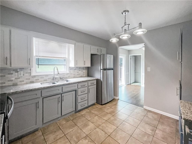 kitchen featuring pendant lighting, a sink, light stone counters, freestanding refrigerator, and decorative backsplash