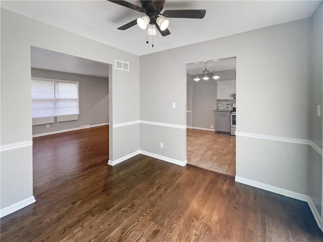 empty room featuring visible vents, dark wood-type flooring, and baseboards