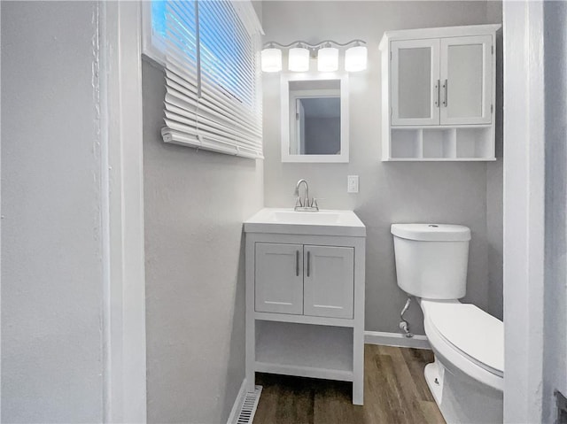 half bathroom featuring toilet, vanity, baseboards, and wood finished floors