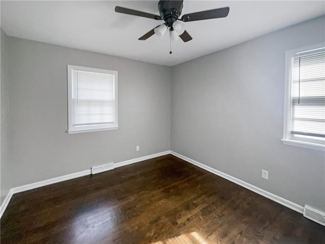 spare room featuring dark wood finished floors, baseboards, visible vents, and a ceiling fan