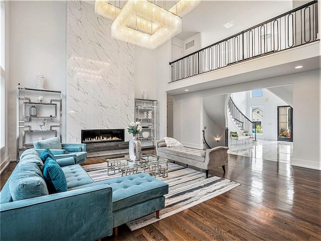 living room featuring a towering ceiling, a notable chandelier, a premium fireplace, and wood-type flooring