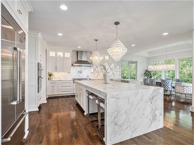 kitchen with decorative light fixtures, wall chimney exhaust hood, white cabinetry, appliances with stainless steel finishes, and dark hardwood / wood-style floors