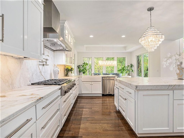 kitchen with hanging light fixtures, wall chimney range hood, white cabinetry, appliances with stainless steel finishes, and dark hardwood / wood-style floors