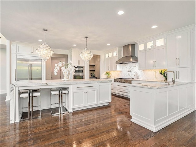 kitchen featuring a notable chandelier, stainless steel appliances, white cabinets, and wall chimney range hood