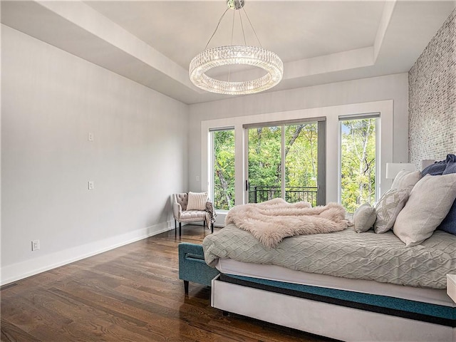 bedroom with a raised ceiling, dark hardwood / wood-style flooring, and a chandelier