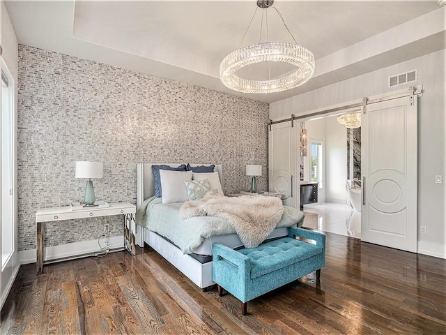 bedroom featuring a barn door, a raised ceiling, an inviting chandelier, and dark hardwood / wood-style floors