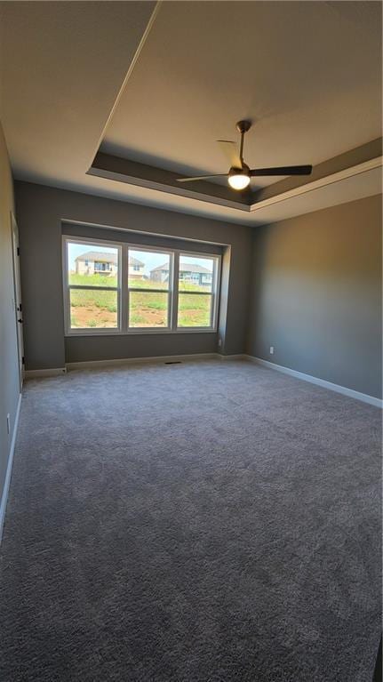 spare room featuring a tray ceiling, baseboards, ceiling fan, and carpet