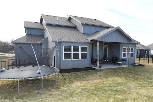 back of house with a trampoline, roof with shingles, a yard, a patio, and fence