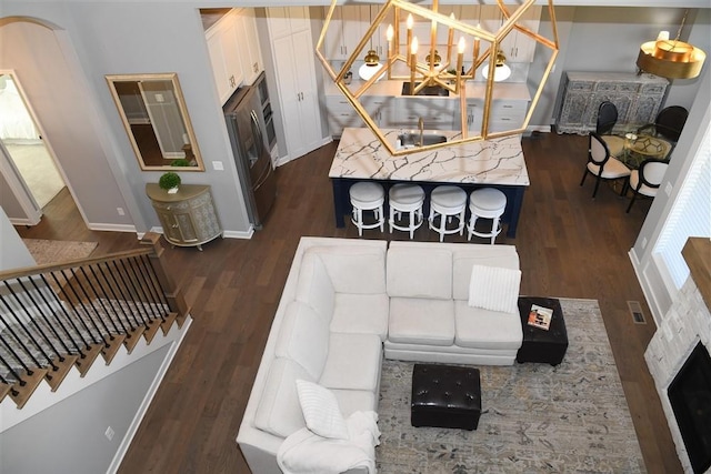 living room featuring dark wood-type flooring, a notable chandelier, stairway, and baseboards