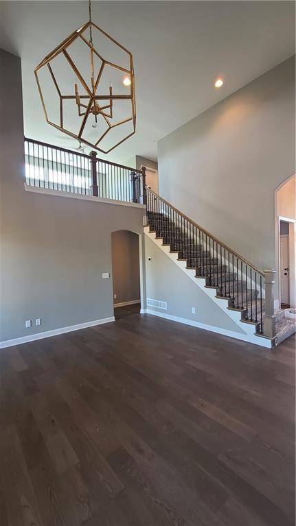 unfurnished living room featuring arched walkways, stairway, baseboards, and wood finished floors