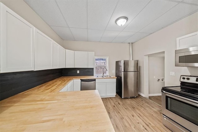 kitchen featuring white cabinets, light wood-style flooring, stainless steel appliances, a paneled ceiling, and a sink