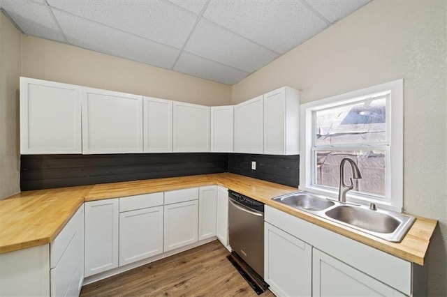 kitchen featuring butcher block counters, a sink, a paneled ceiling, white cabinetry, and stainless steel dishwasher