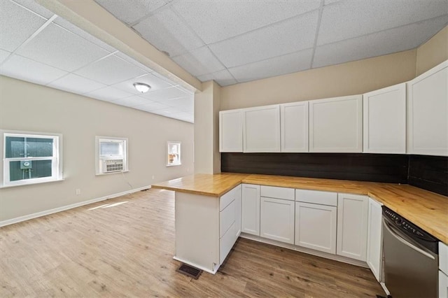 kitchen with a drop ceiling, open floor plan, light wood-type flooring, wooden counters, and stainless steel dishwasher