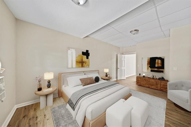 bedroom featuring a drop ceiling, wood finished floors, and baseboards