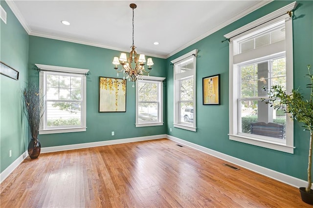 empty room with light hardwood / wood-style floors, crown molding, a healthy amount of sunlight, and a notable chandelier