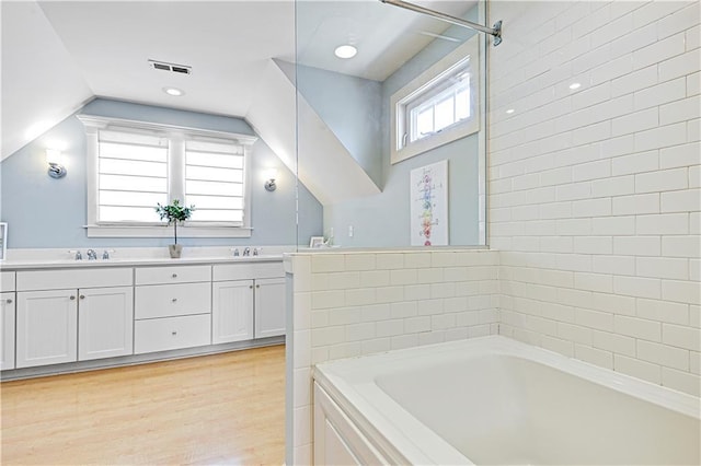 bathroom with a tub to relax in, vanity, wood-type flooring, and lofted ceiling