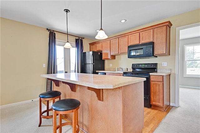 kitchen with a breakfast bar, a center island, black appliances, hanging light fixtures, and light hardwood / wood-style floors