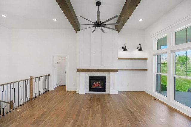 unfurnished living room with a towering ceiling, beamed ceiling, light wood-type flooring, and ceiling fan