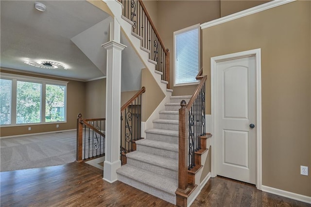 stairs with wood-type flooring, crown molding, and decorative columns