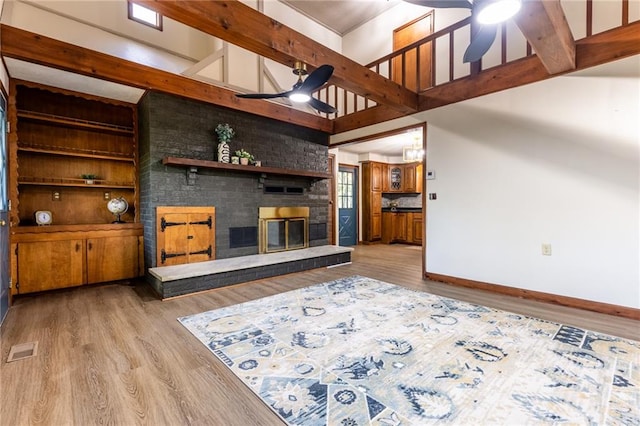 living room featuring ceiling fan, beam ceiling, wood-type flooring, and a brick fireplace