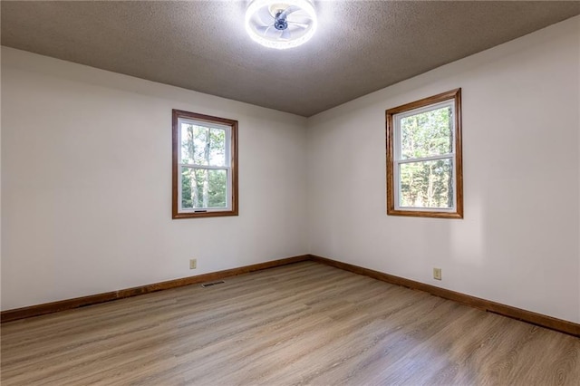 empty room with light wood-style floors, baseboards, and a textured ceiling