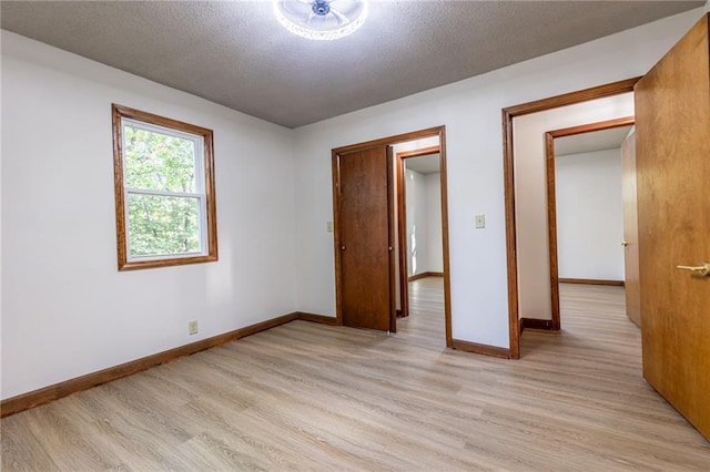 unfurnished bedroom featuring baseboards, a textured ceiling, and light wood-style floors