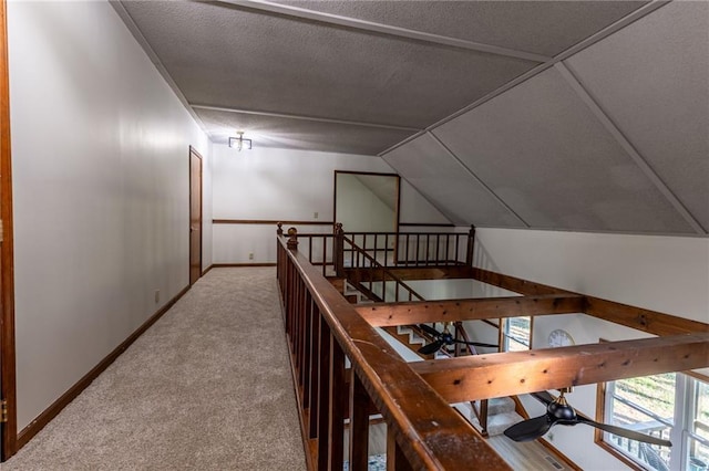 hall with an upstairs landing, carpet flooring, baseboards, and vaulted ceiling