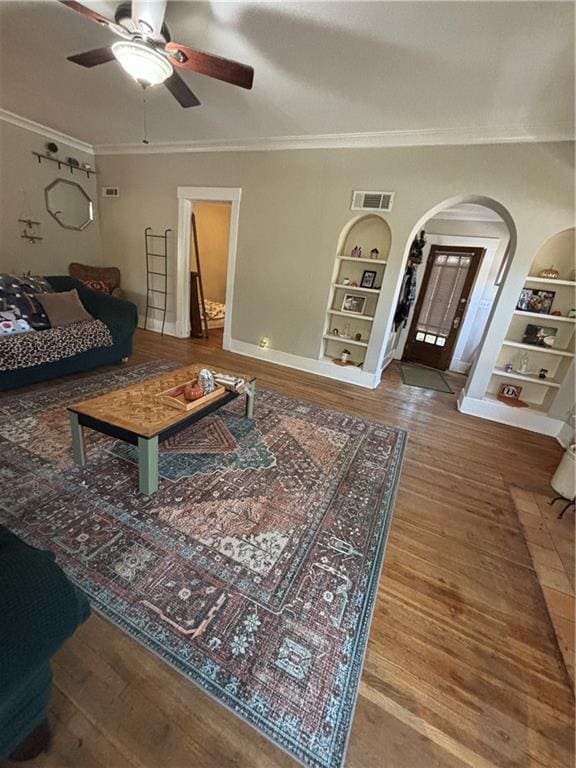 living room featuring built in shelves, ceiling fan, wood-type flooring, and crown molding