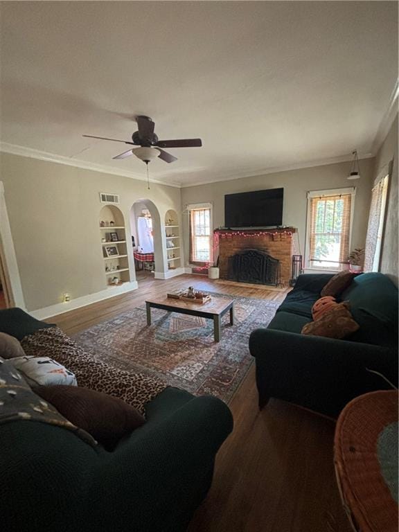 living room with built in shelves, hardwood / wood-style flooring, ceiling fan, and ornamental molding