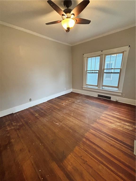 unfurnished room with visible vents, a ceiling fan, ornamental molding, baseboards, and dark wood-style flooring