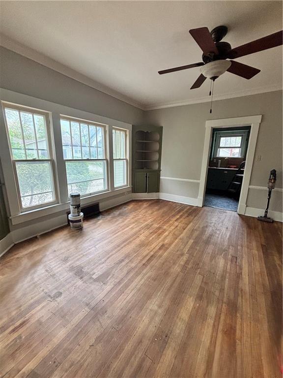 interior space with baseboards, crown molding, hardwood / wood-style flooring, and a ceiling fan