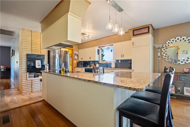 kitchen featuring black appliances, pendant lighting, hardwood / wood-style floors, kitchen peninsula, and stone counters