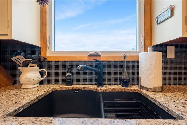 interior details with sink, light stone countertops, and backsplash