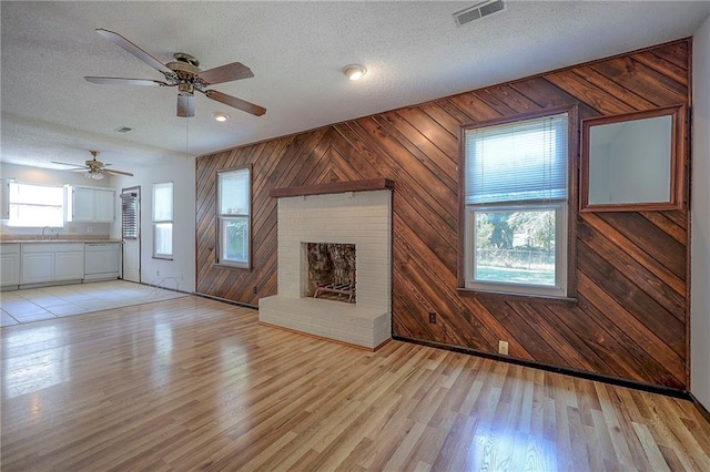 unfurnished living room with a textured ceiling, a wealth of natural light, light hardwood / wood-style flooring, and ceiling fan