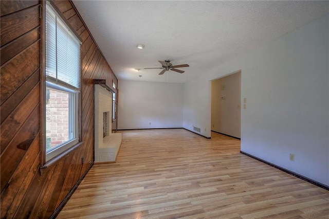 interior space featuring a textured ceiling, light hardwood / wood-style flooring, ceiling fan, and wooden walls