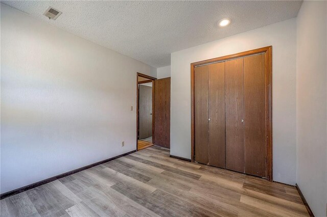 unfurnished bedroom with a closet, a textured ceiling, and light hardwood / wood-style flooring