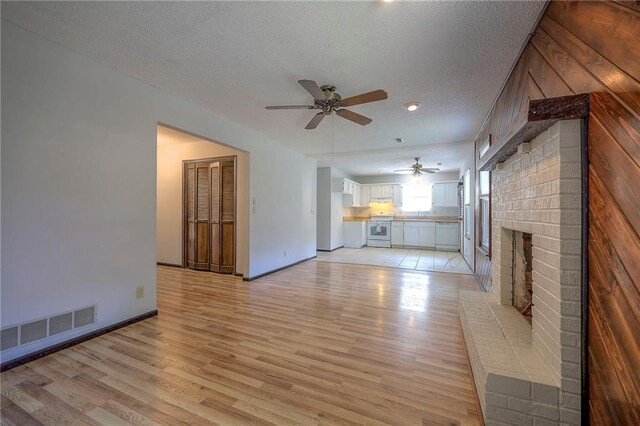 unfurnished living room featuring a fireplace, wooden walls, a textured ceiling, light hardwood / wood-style flooring, and ceiling fan