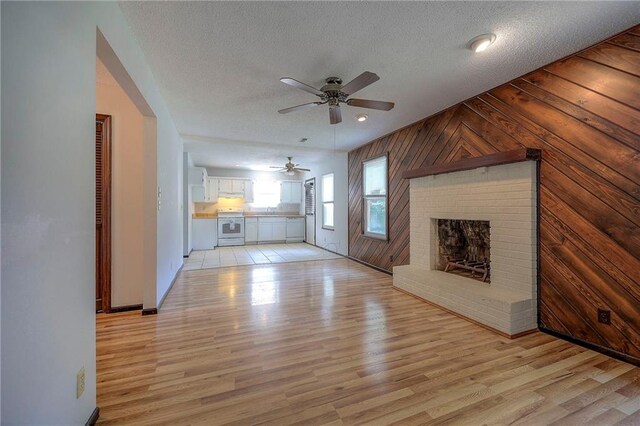 unfurnished living room featuring light wood-type flooring, a textured ceiling, a fireplace, and ceiling fan