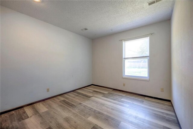 spare room with light wood-type flooring and a textured ceiling