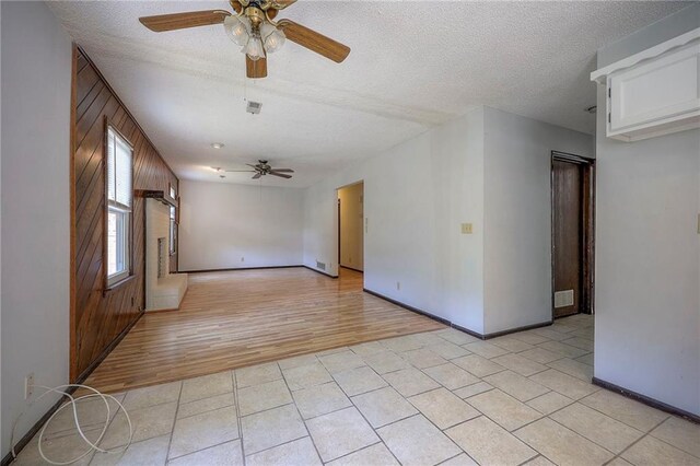 spare room featuring light wood-type flooring, wood walls, ceiling fan, and a textured ceiling