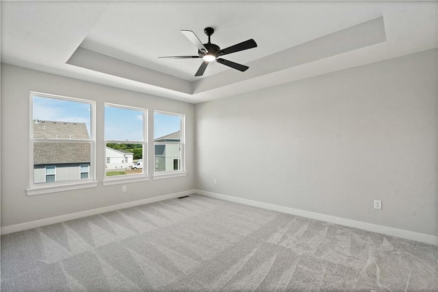 unfurnished room with visible vents, a tray ceiling, carpet flooring, baseboards, and ceiling fan