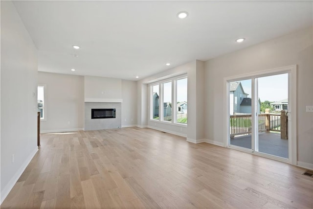 unfurnished living room featuring a glass covered fireplace, baseboards, light wood-style flooring, and recessed lighting