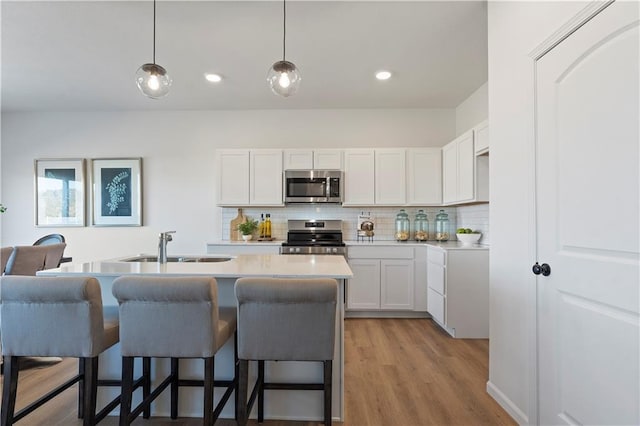 kitchen with hanging light fixtures, light hardwood / wood-style flooring, backsplash, white cabinets, and appliances with stainless steel finishes