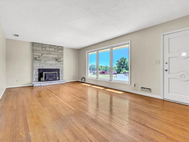 unfurnished living room featuring a fireplace, light wood-type flooring, and a textured ceiling