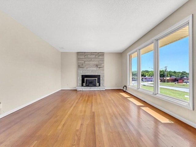 unfurnished living room with a textured ceiling, a stone fireplace, and light wood-type flooring