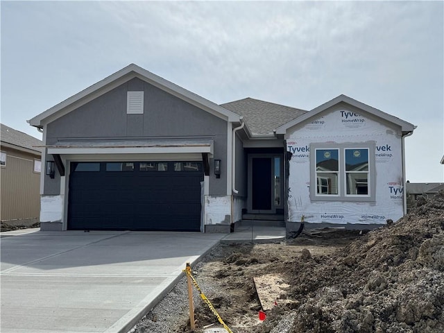 unfinished property featuring driveway, roof with shingles, and an attached garage