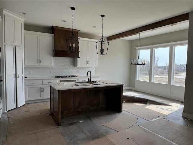 kitchen with tasteful backsplash, white cabinets, hanging light fixtures, a sink, and beam ceiling