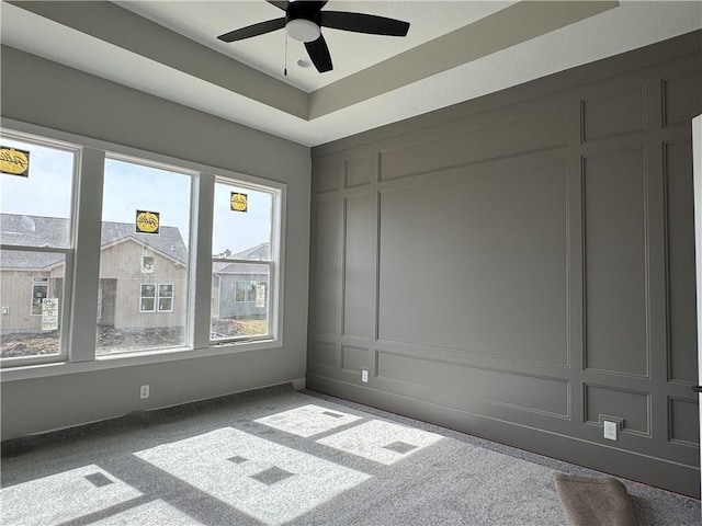 carpeted spare room with a ceiling fan, a raised ceiling, and a decorative wall