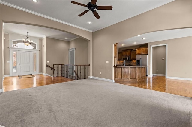 unfurnished living room featuring ornamental molding, ceiling fan with notable chandelier, and light carpet